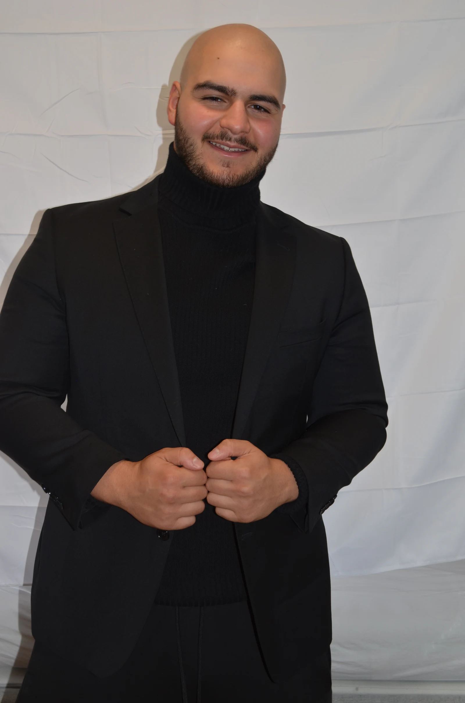 Deniz lächelt im schwarzen Sakko und hält die Revers fest.