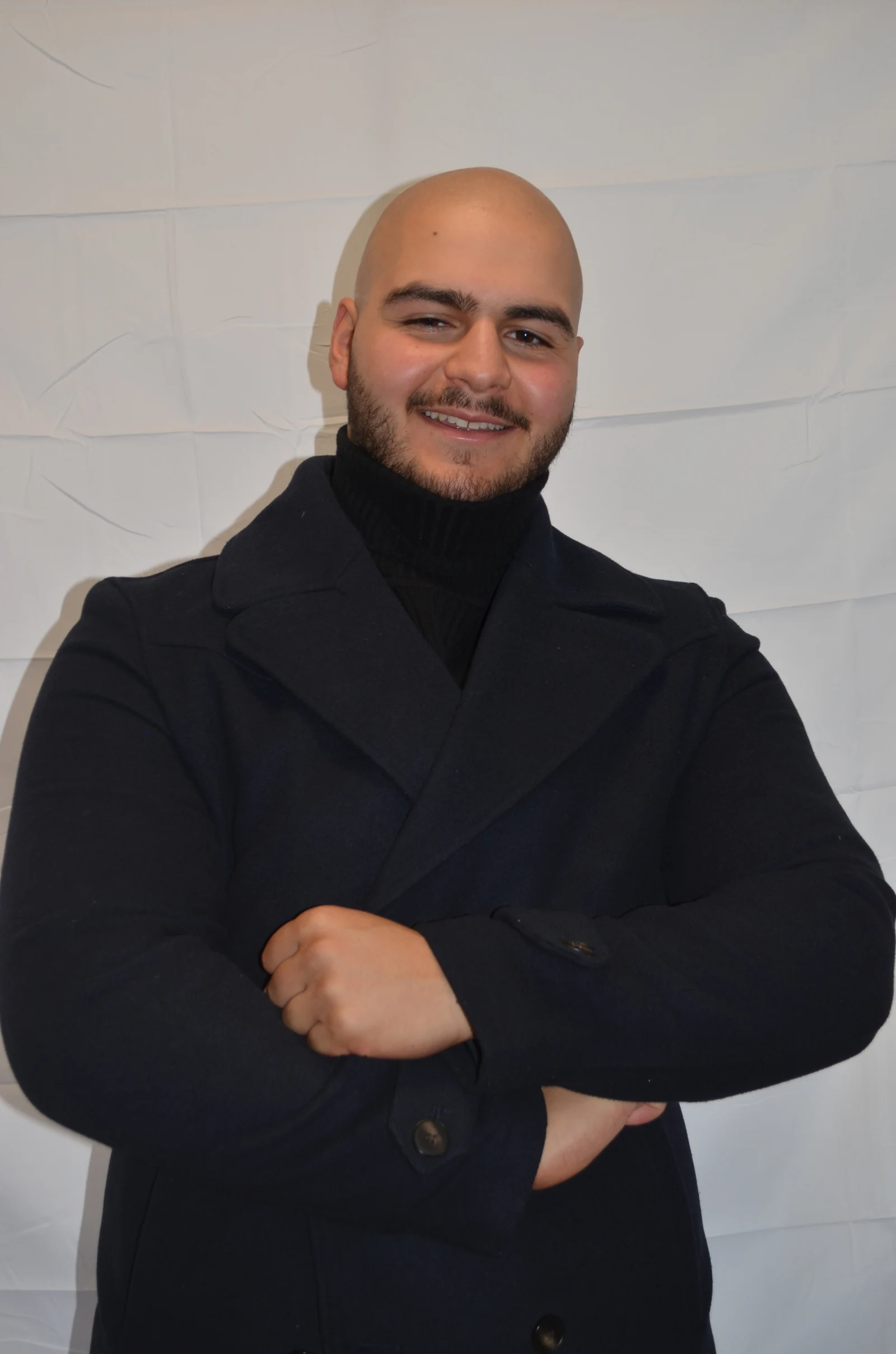 Deniz im schwarzen Sakko, lächelnd im Studio.